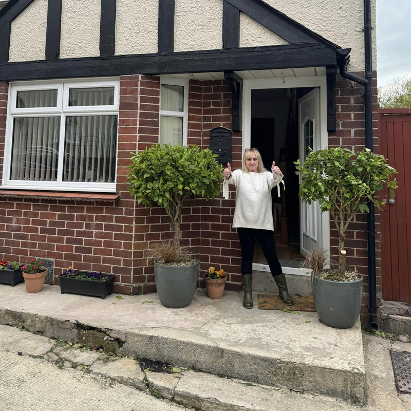 Happy homeowner holding thumbs up outside her house